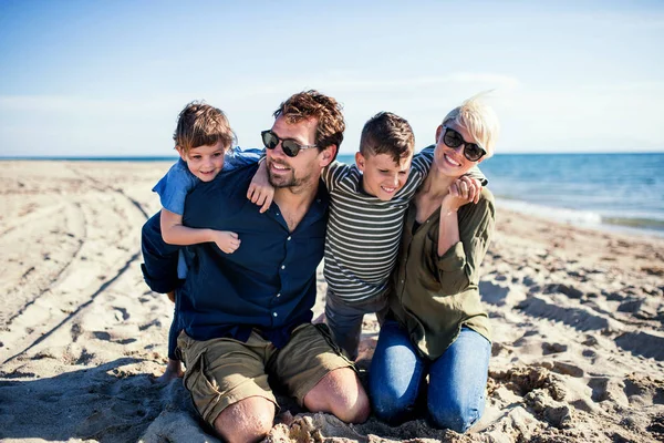 Νεαρή οικογένεια με δύο μικρά παιδιά που κάθονται στην παραλία. — Φωτογραφία Αρχείου