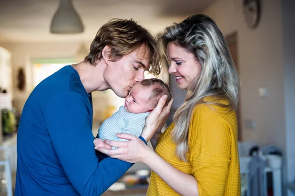 Belos pais jovens com um bebê recém-nascido em casa, beijando . — Fotografia de Stock