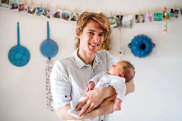 Um jovem pai segurando um bebê recém-nascido em casa . — Fotografia de Stock