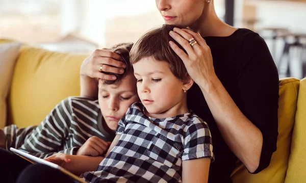 Een jonge vrouw met twee kinderen binnenshuis thuis, met behulp van Tablet. — Stockfoto