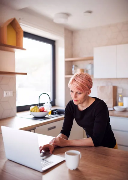 Uma jovem mulher usando laptop em uma cozinha em casa . — Fotografia de Stock
