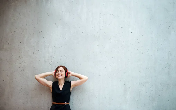 Młody biznes kobieta ze słuchawkami stojące przed betonowe ściany w biurze. — Zdjęcie stockowe