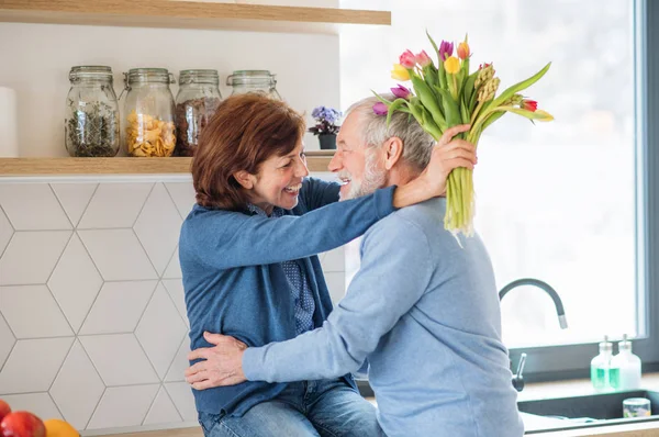 Um casal de idosos apaixonado dentro de casa, homem dando flores para a mulher . — Fotografia de Stock