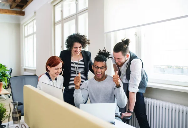 Grupo de jóvenes empresarios alegres utilizando el ordenador portátil en la oficina, concepto de puesta en marcha . — Foto de Stock