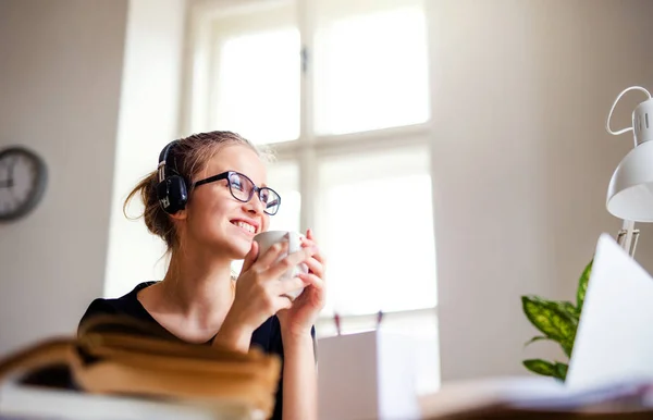 En ung kvinnlig elev som sitter vid bordet, använder hörlurar när man studerar. — Stockfoto