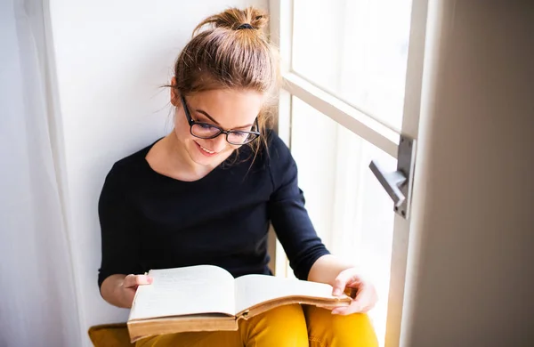 Eine junge Studentin mit Buch sitzt auf dem Fensterbrett und studiert. — Stockfoto