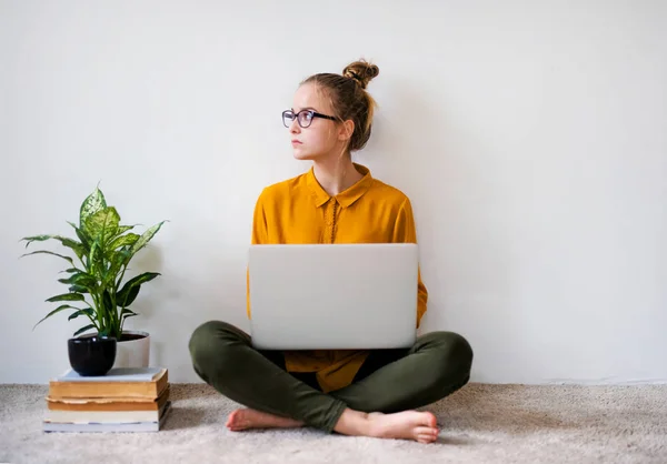 En ung kvinnlig student sitter på golvet med hjälp av laptop när man studerar. — Stockfoto