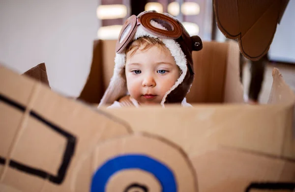 Een peuter meisje met kartonnen vliegtuig spelen binnenshuis thuis, Flying concept. — Stockfoto