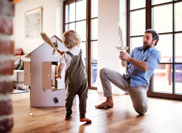 Un niño y un padre con espadas de cartón jugando en casa . — Foto de Stock