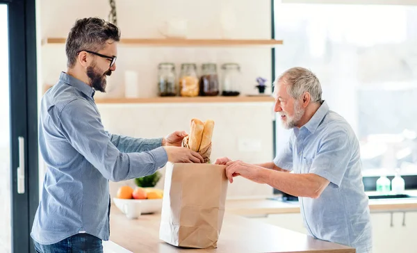 En vuxen hipster son och Senior far inomhus hemma, uppackning shopping. — Stockfoto