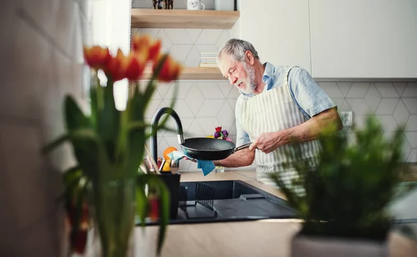 Um homem sênior dentro de casa na cozinha, lavando a louça uma panela . — Fotografia de Stock