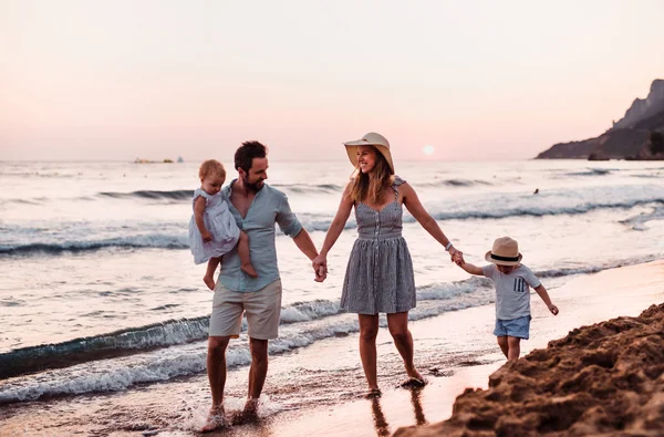 Giovane famiglia con due bambini piccoli che camminano sulla spiaggia in vacanza estiva . — Foto Stock