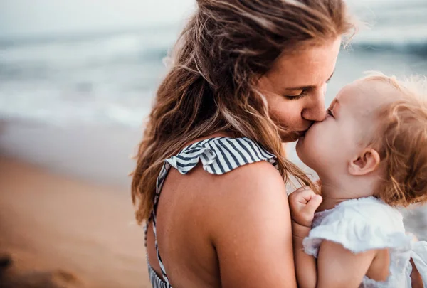 Közeli fel a fiatal anya egy kisgyermek lány a strandon a nyári szünet, csókolózás. — Stock Fotó