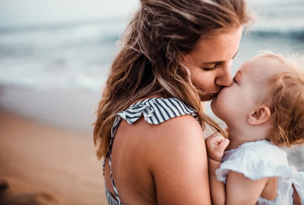 Primer plano de la madre joven con una niña en la playa en las vacaciones de verano, besándose . — Foto de Stock