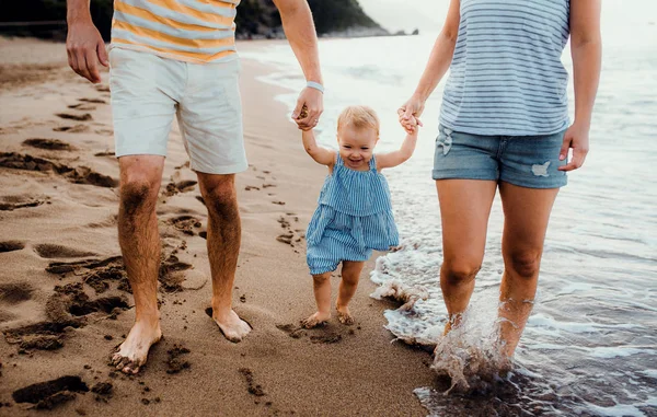 Una sezione centrale dei genitori con la figlia del bambino che cammina sulla spiaggia in vacanza estiva . — Foto Stock
