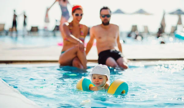 Un bambino piccolo con bracciali e genitori in piscina in vacanza estiva . — Foto Stock