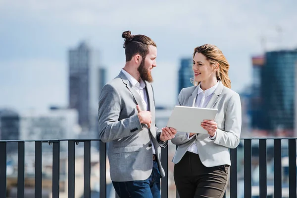 Zwei junge Geschäftsleute mit Tablet stehen auf einer Terrasse vor dem Büro und arbeiten. — Stockfoto