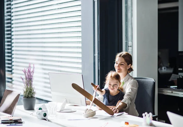 Eine Geschäftsfrau mit kleiner Tochter sitzt in einem Büro, arbeitet und spielt. — Stockfoto