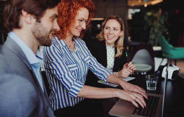 A group of young business people with laptop sitting in an office, talking. — Stock Photo, Image