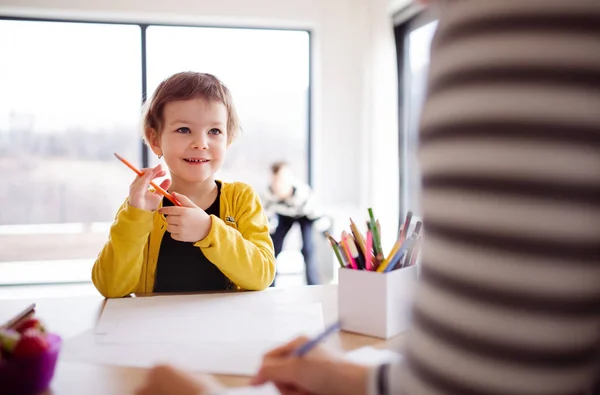 Een klein meisje met onherkenbaar moeder tekening in een keuken. — Stockfoto