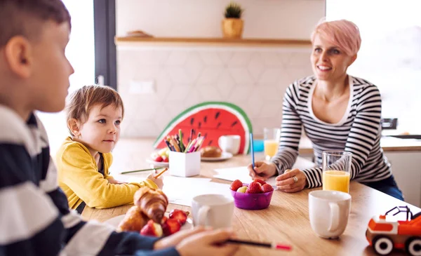 A young woman with two children drawing in a kitchen. — Stock Photo, Image