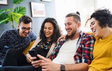 Kapalı kanepede oturan akıllı telefon ile genç arkadaş bir grup, ev paylaşım konsepti.