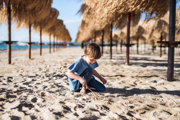 Una niña pequeña jugando entre sombrillas de paja al aire libre en la playa . — Foto de Stock