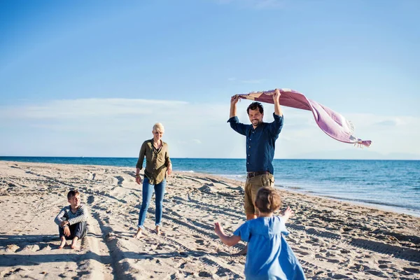 Junge Familie mit zwei kleinen Kindern geht draußen am Strand spazieren. — Stockfoto