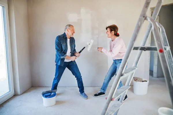 Pareja mayor pintando paredes en un nuevo hogar, divirtiéndose. Concepto de reubicación . — Foto de Stock