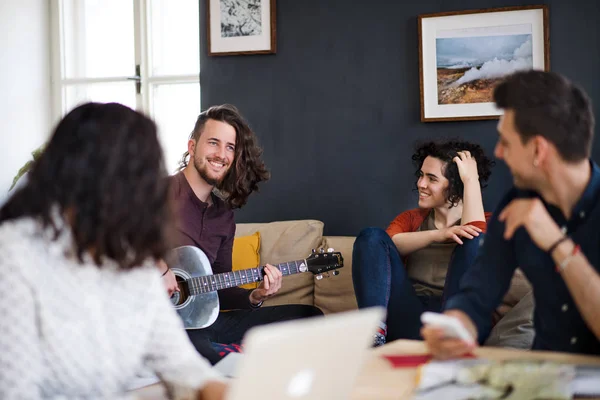 A group of young friends with guitar indoors at home, house sharing concept. — Stock Photo, Image