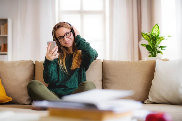 Uma jovem estudante sentada no sofá, usando fones de ouvido ao estudar . — Fotografia de Stock