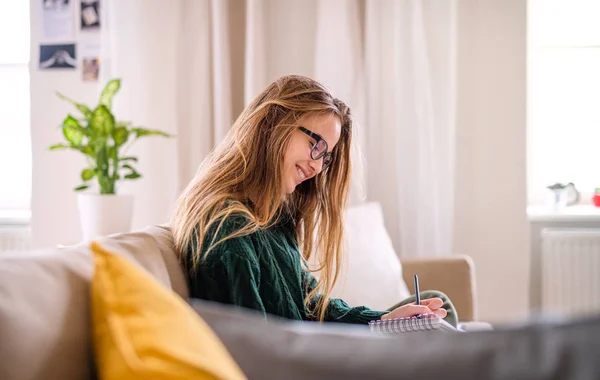 Eine glückliche junge Studentin sitzt auf dem Sofa und studiert. — Stockfoto