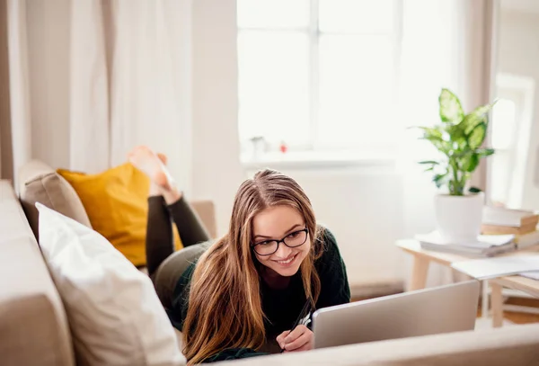 Eine junge Studentin liegt auf dem Sofa und benutzt Laptop während des Studiums. — Stockfoto