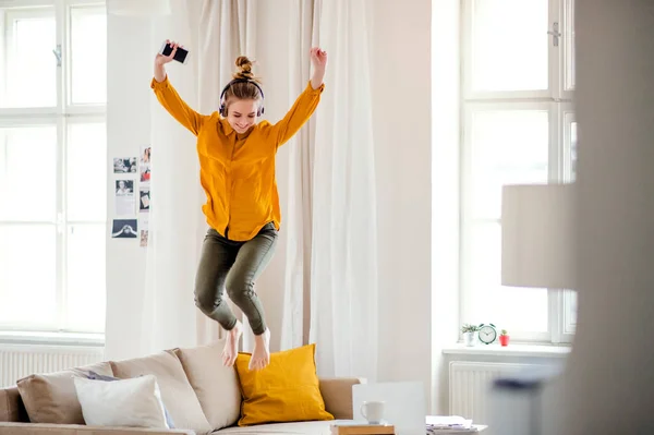 Una giovane studentessa con le cuffie che salta sul divano mentre studia . — Foto Stock