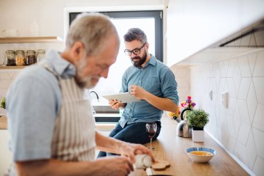 Yetişkin hipster oğlu ve üst düzey baba evde mutfakta kapalı, tablet kullanarak.