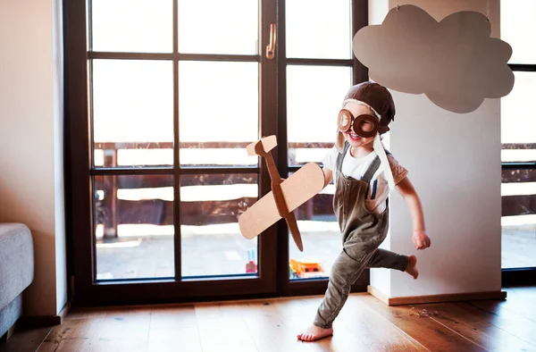 Un tout-petit garçon avec un avion en carton jouant à l'intérieur à la maison, concept volant . — Photo