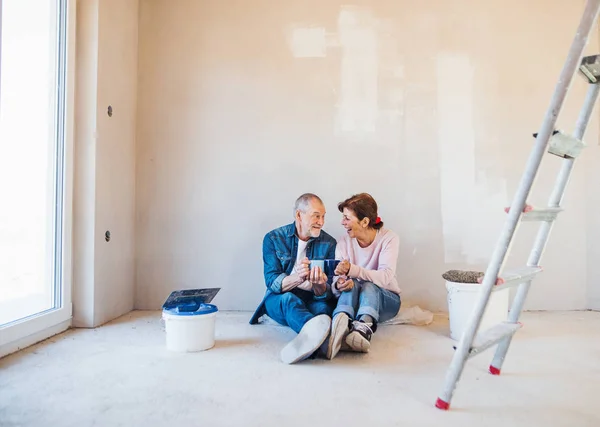 Starší dvojice maluje zdi v novém domově a odpočívá. Koncepce přemístění. — Stock fotografie
