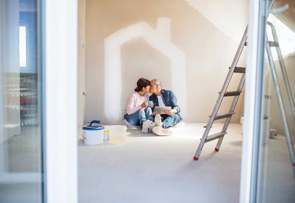 Pareja mayor pintando paredes en casa nueva, besándose. Concepto de reubicación . — Foto de Stock