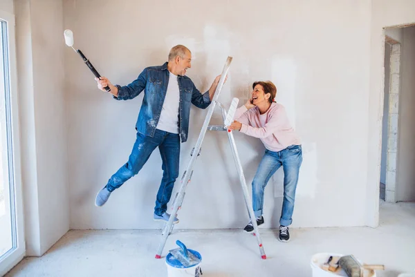 Pareja mayor pintando paredes en un nuevo hogar, divirtiéndose. Concepto de reubicación . —  Fotos de Stock