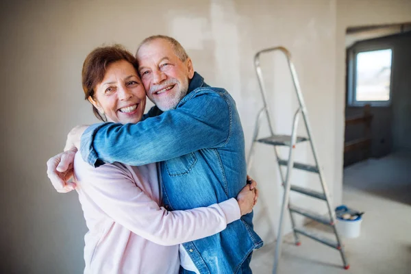 Casal sênior pintando paredes em casa nova, abraçando. Conceito de recolocação . — Fotografia de Stock