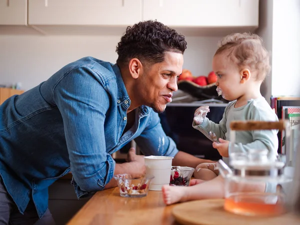 Un padre y un pequeño hijo comiendo fruta y yogur en casa . —  Fotos de Stock