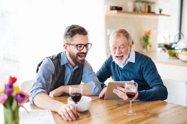 Adulto filho hipster e pai sênior sentado na mesa dentro de casa . — Fotografia de Stock