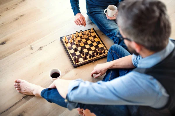 Un milieu de fils adulte et père aîné assis sur le sol à l'intérieur, jouant aux échecs . — Photo