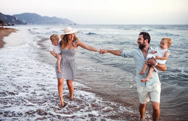 Giovane famiglia con due bambini piccoli che camminano sulla spiaggia in vacanza estiva . — Foto Stock