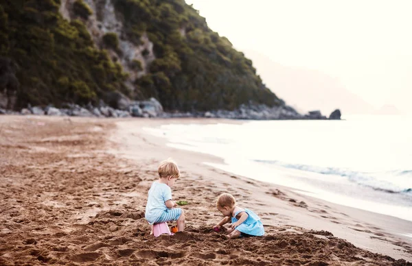 Dua anak kecil bermain di pantai pasir saat liburan musim panas . — Stok Foto