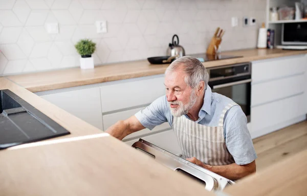 Старший мужчина дома на кухне, загружает посудомоечную машину . — стоковое фото