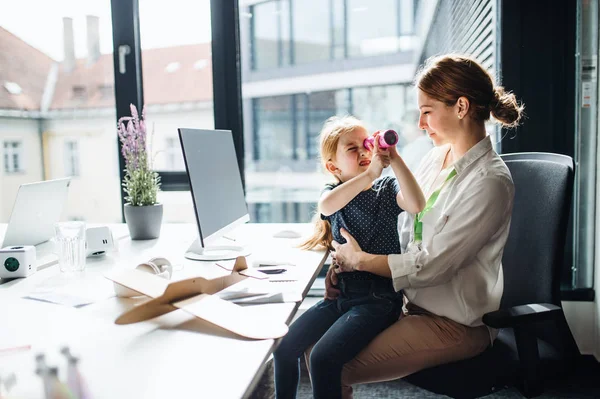 Obchodná žena s malou dcerou, která sedí v kanceláři a pracuje. — Stock fotografie