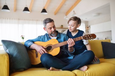 Küçük oğlu ile olgun baba kanepede kapalı oturan, gitar çalıyor.