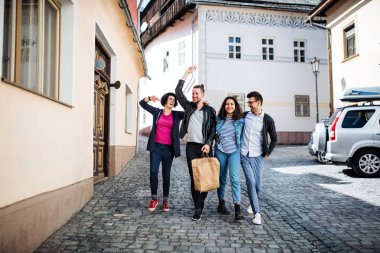 Bir grup genç arkadaş şehirde açık havada yürürken, konuşuyorlar..