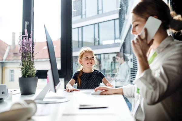Eine Geschäftsfrau mit kleiner Tochter sitzt in einem Büro und arbeitet. — Stockfoto